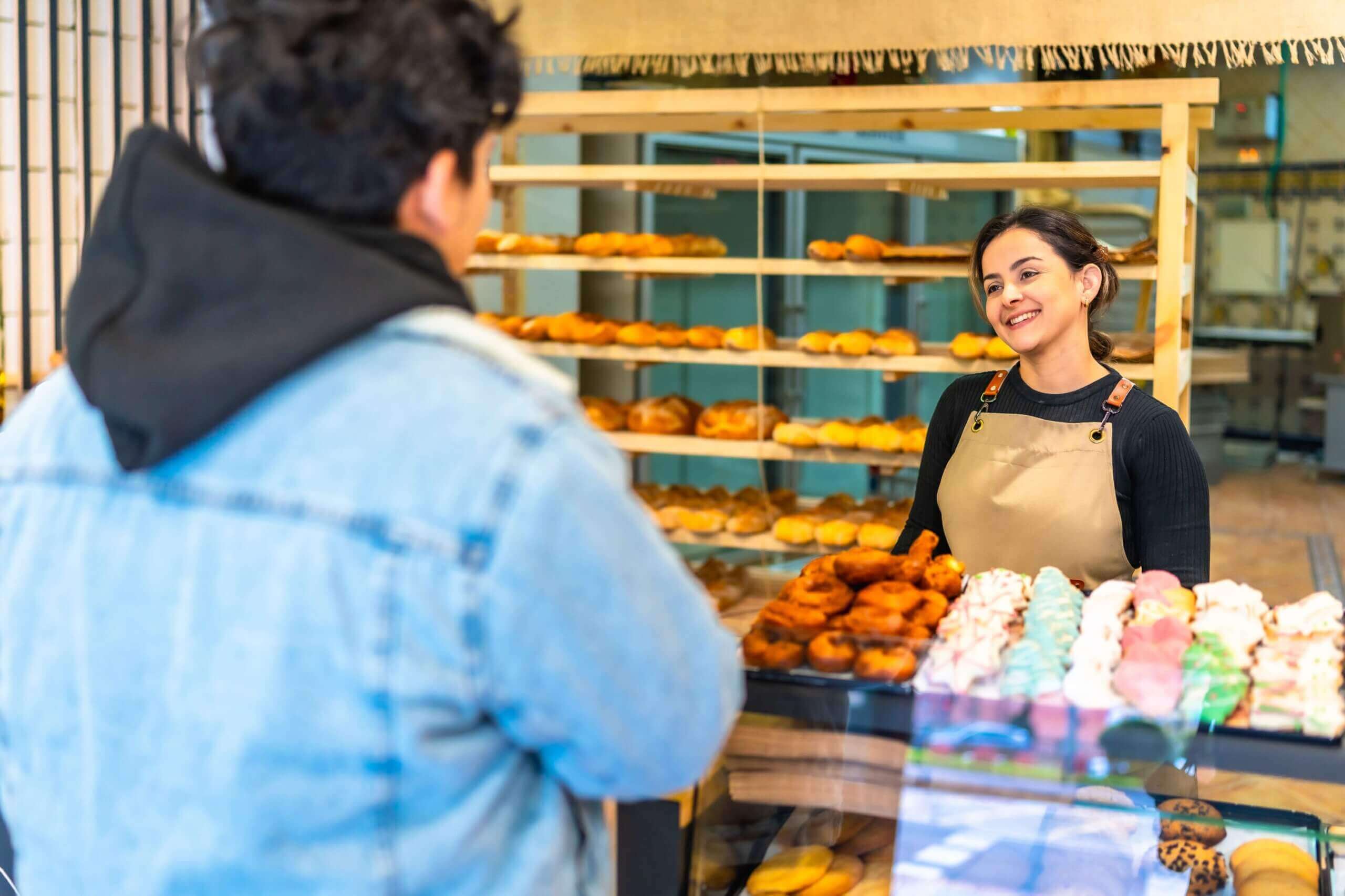 A man purchases baked goods from an artisan bakery, being assisted by a friendly saleswoman