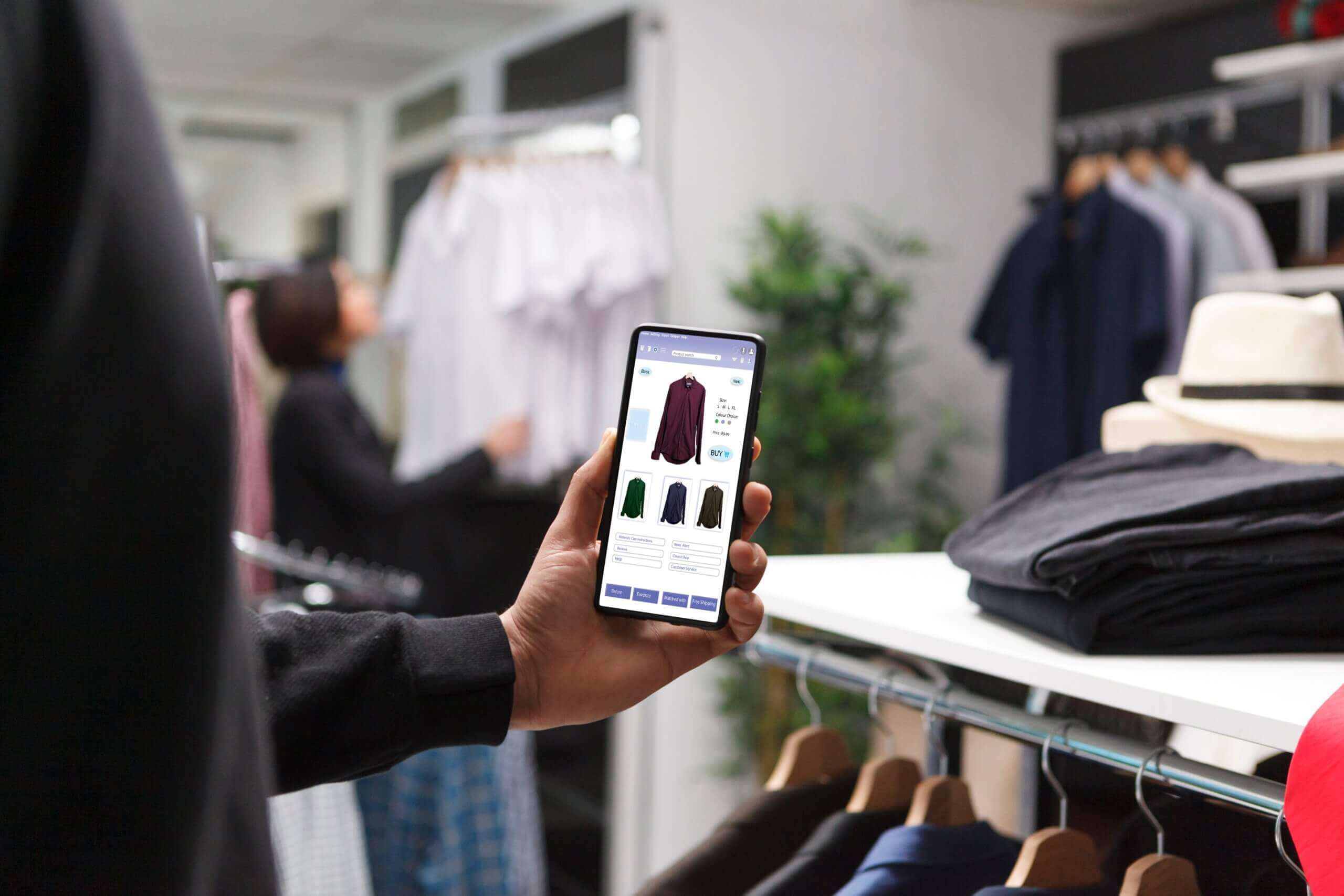 Close-up of a hand holding a phone showing a product page while in a clothing store