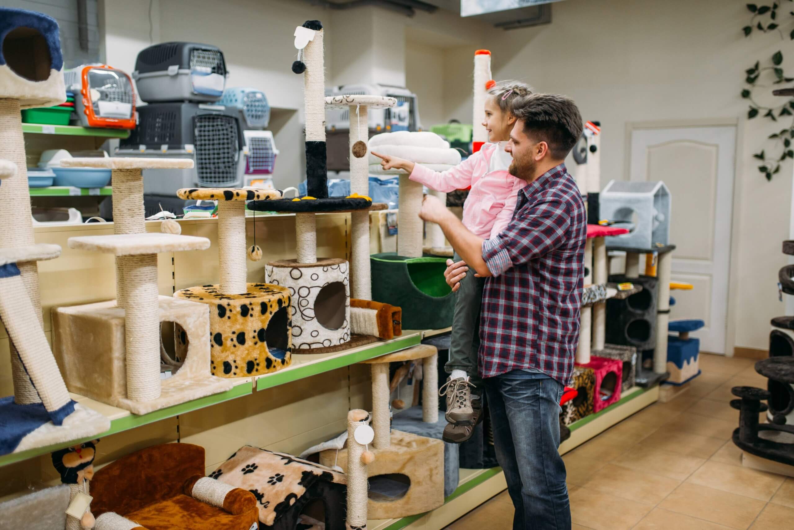  A man and a young girl shopping for cat furniture in a pet store. The shelves are filled with various cat trees, scratching posts, and cozy pet houses in different colors and designs.