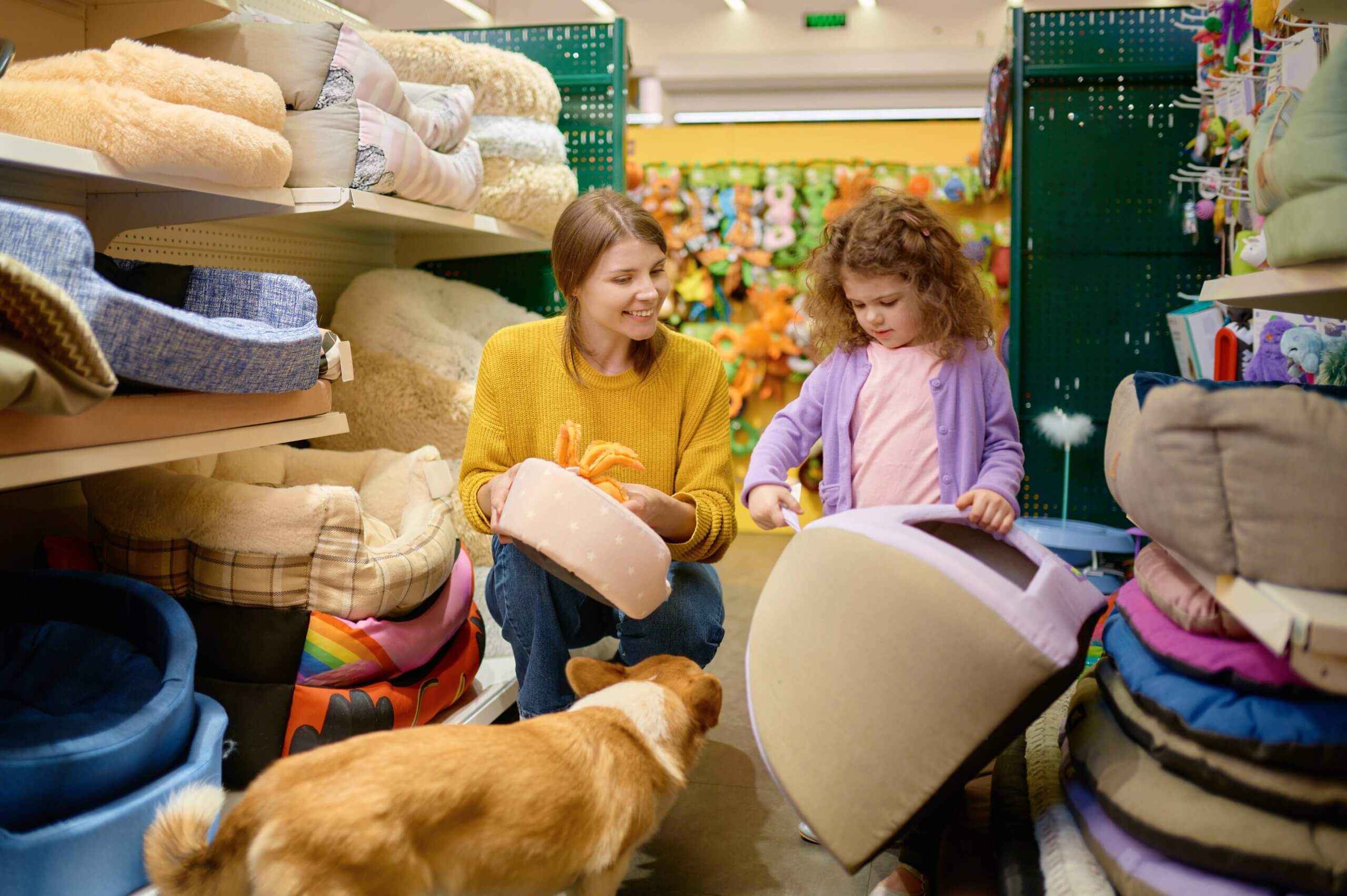  A woman and a girl examine various dog beds in a pet shop, showcasing their interest in pet care and comfort.