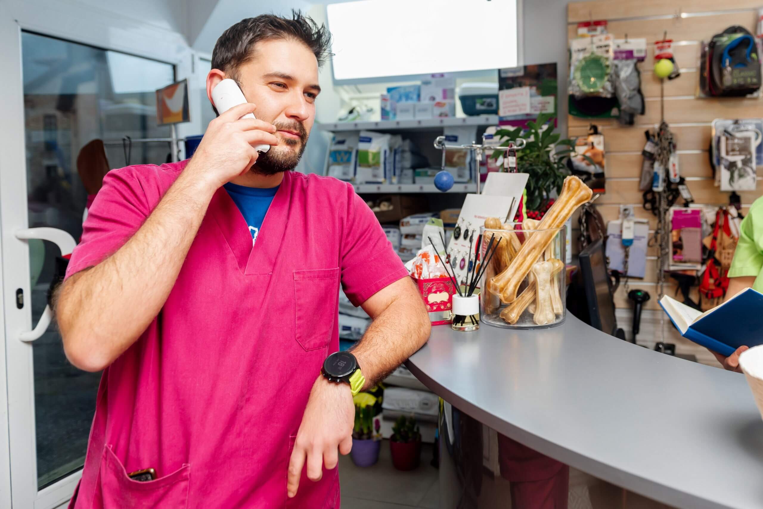 A pet store employee in a pink scrub is engaged in a conversation on his cell phone