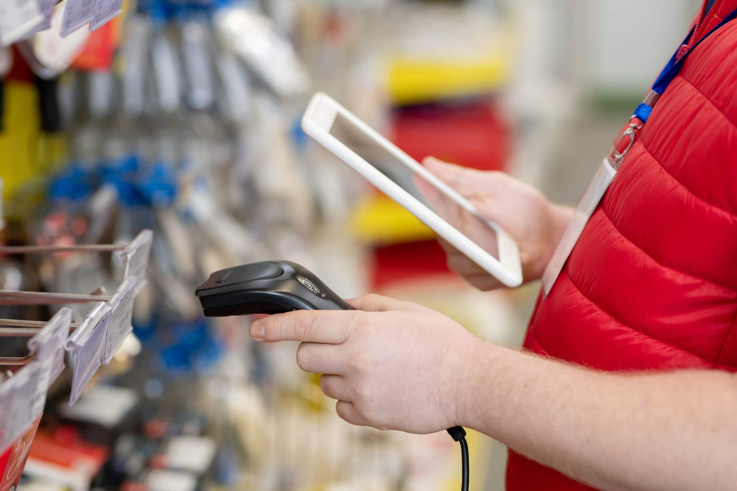 A man in a red vest uses a tablet to conduct an inventory check at a pet store, utilizing a barcode reader