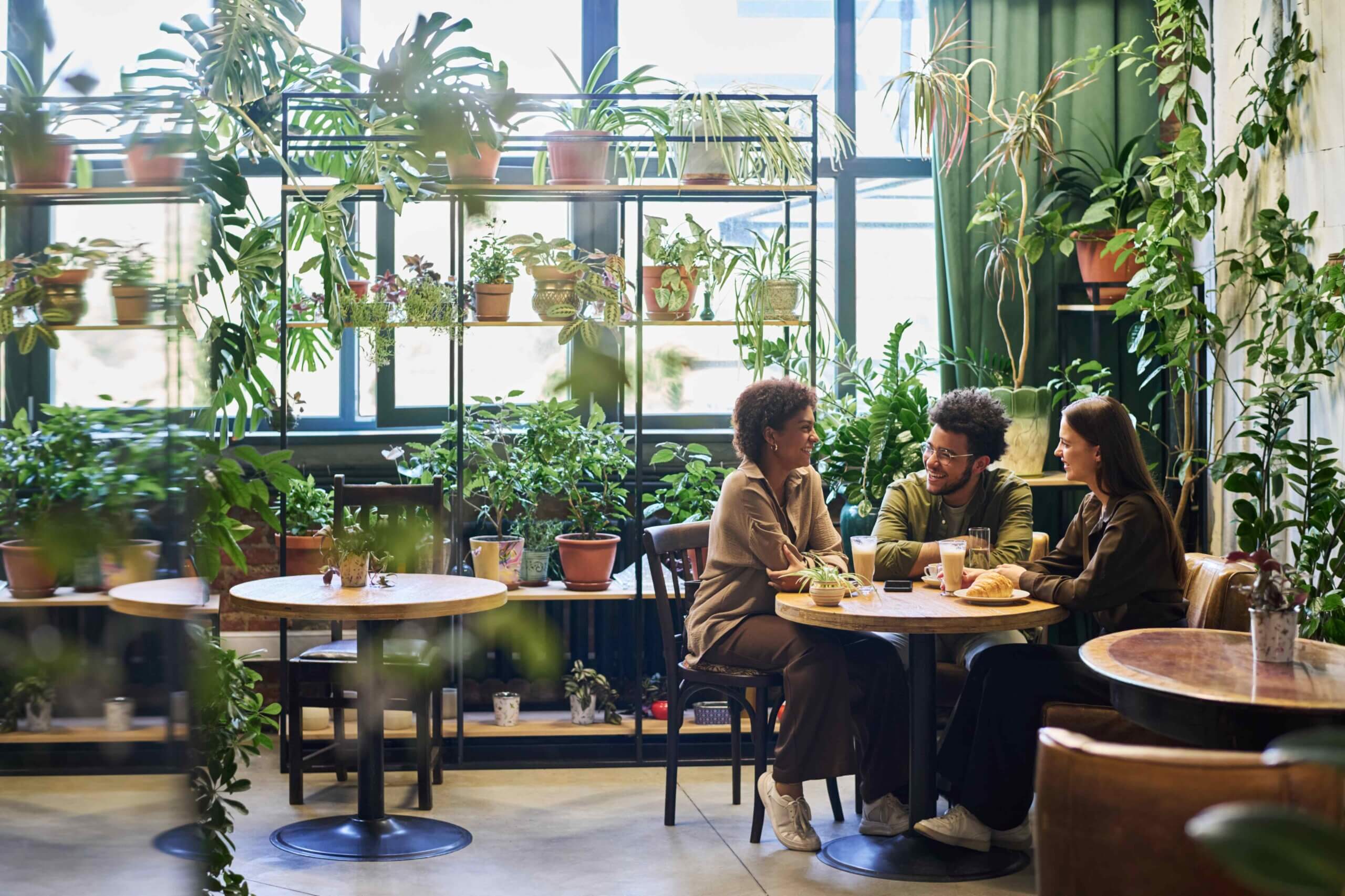 Group of friends sitting by table in the corner of eco friendly cafe with green plants