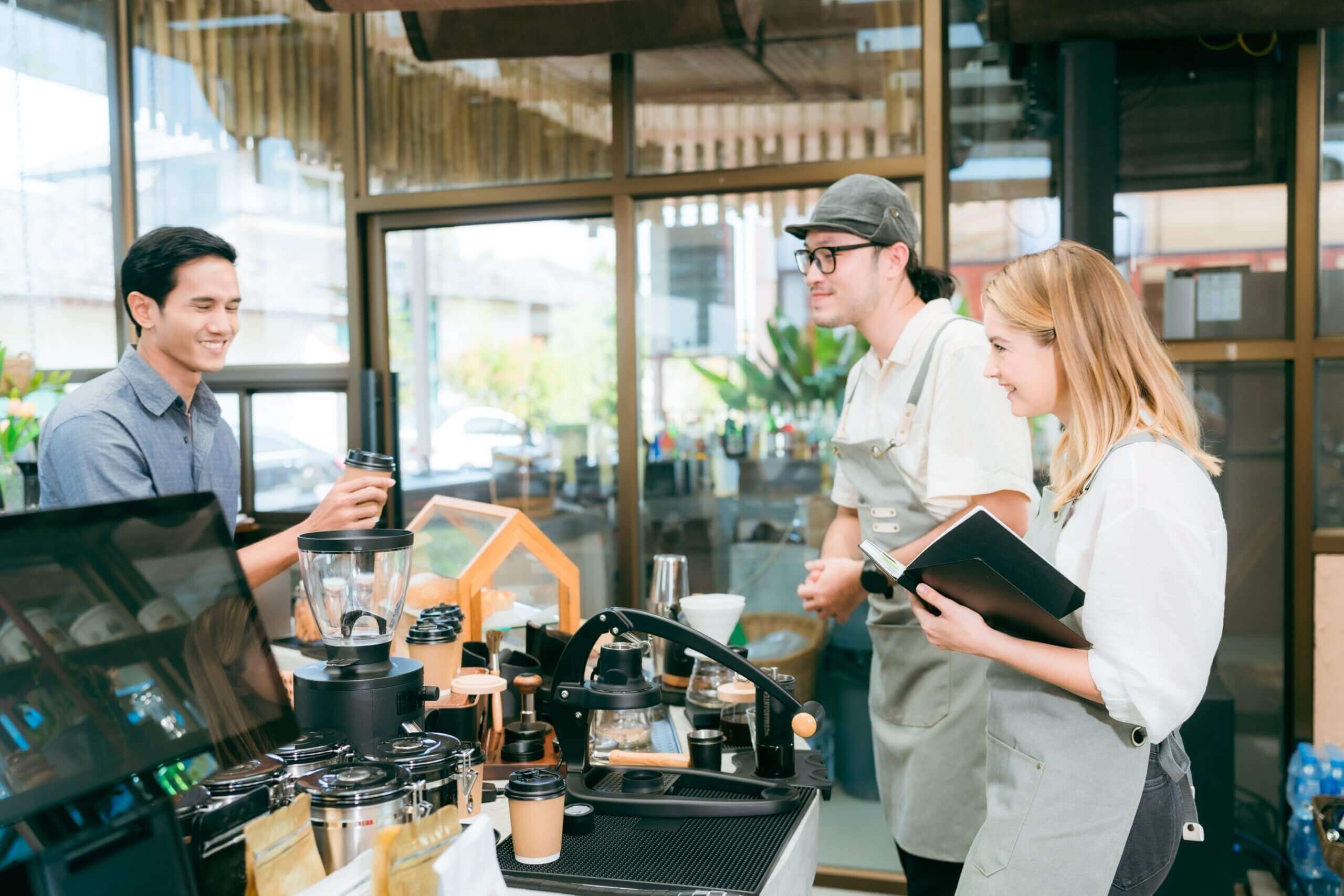 A customer smiles as a barista hands them a takeaway coffee cup at a cozy, modern café with a well-equipped counter